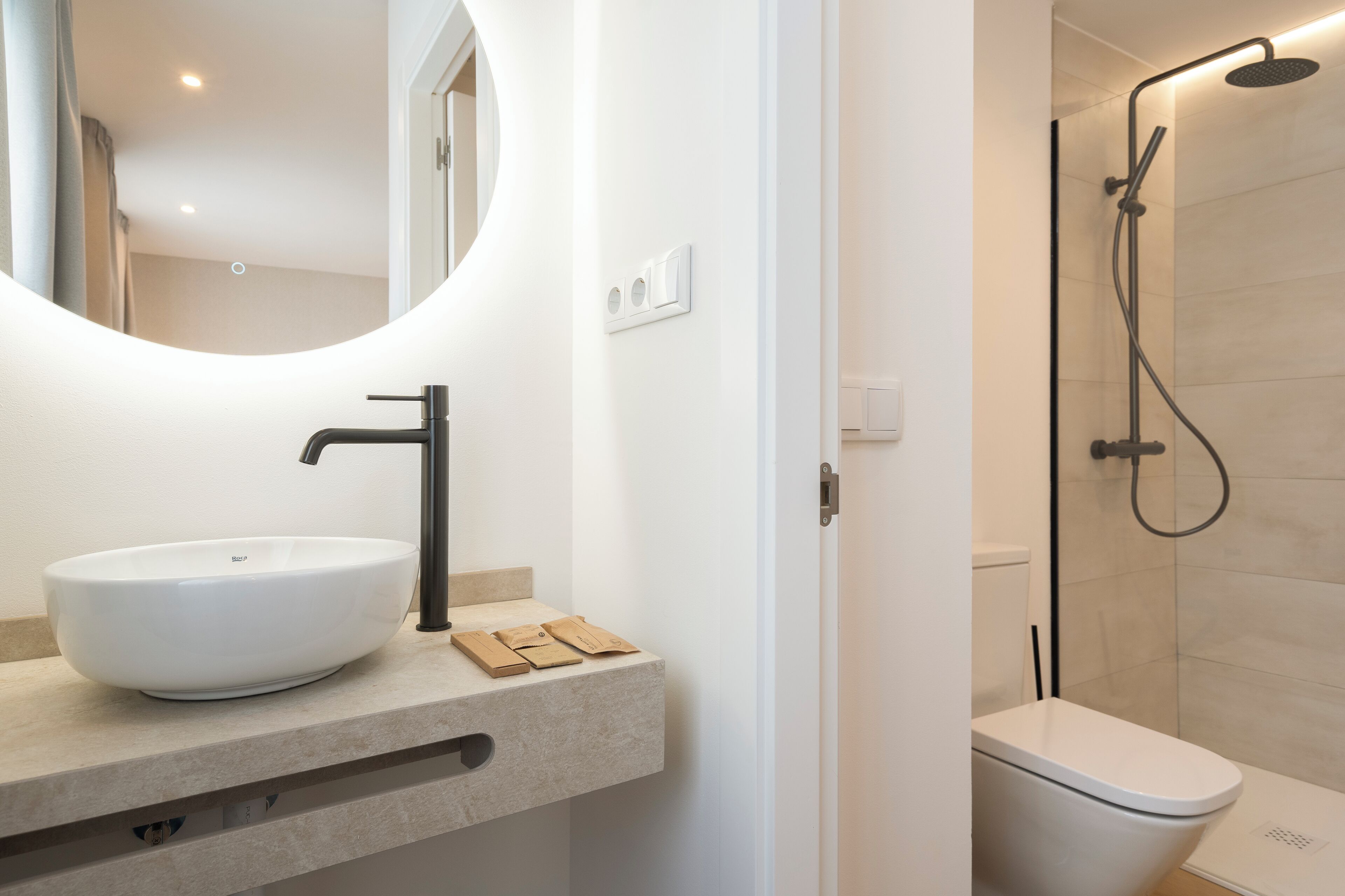 A modern bathroom with a round mirror, a white sink, and a shower enclosure.