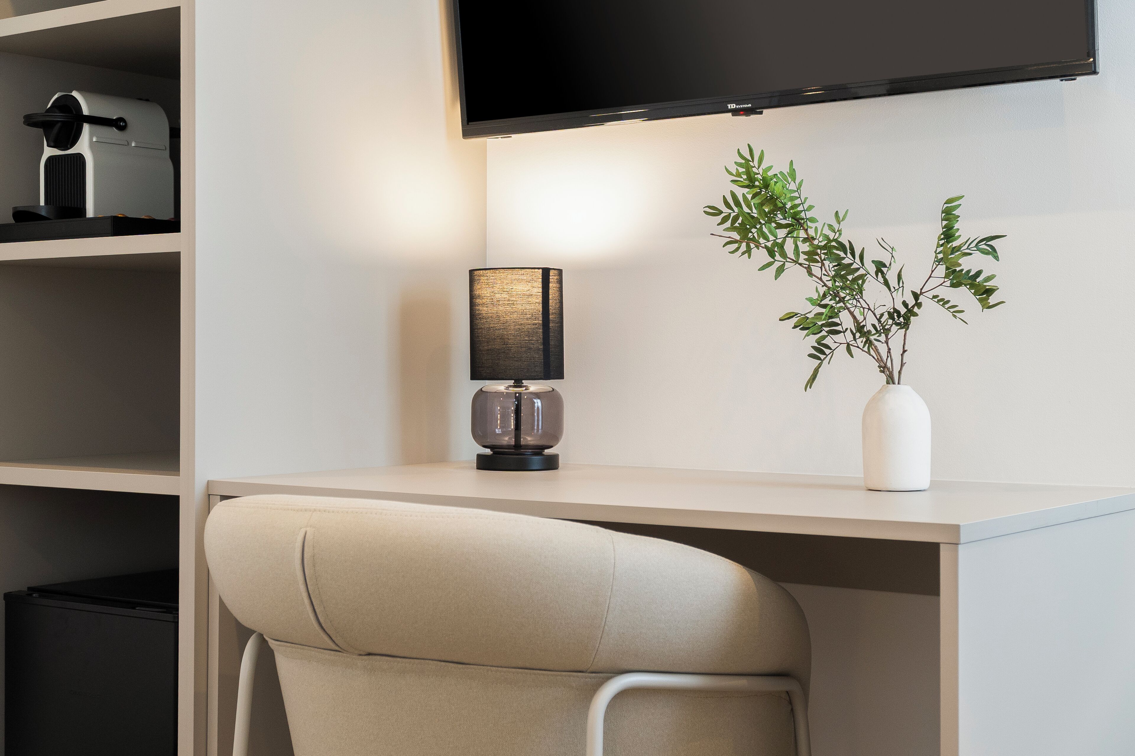 A modern office desk with a lamp, a potted plant, and a flat-screen TV mounted on the wall.