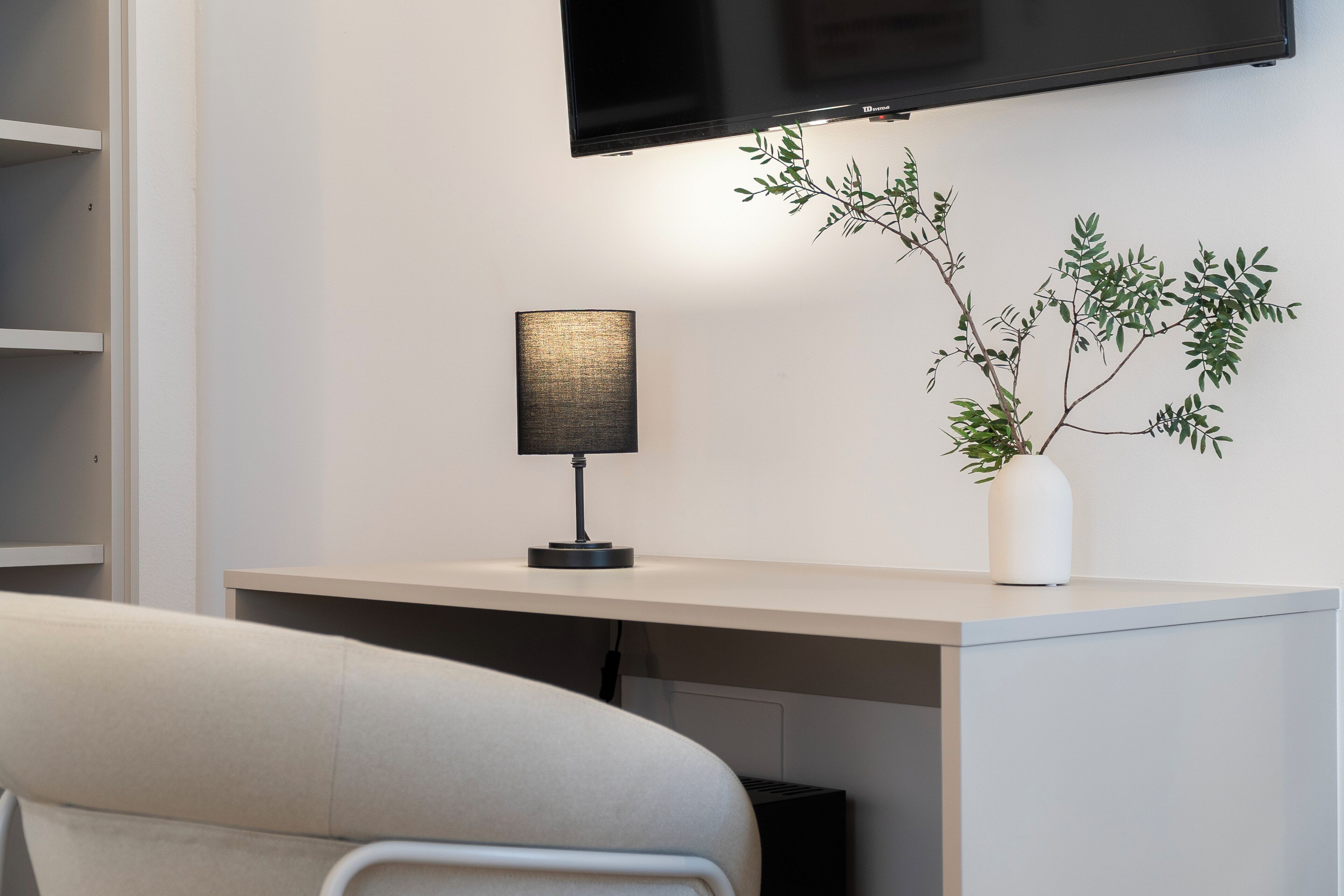 Uma secretária moderna com uma lâmpada, um vaso branco com uma planta e uma televisão montada.