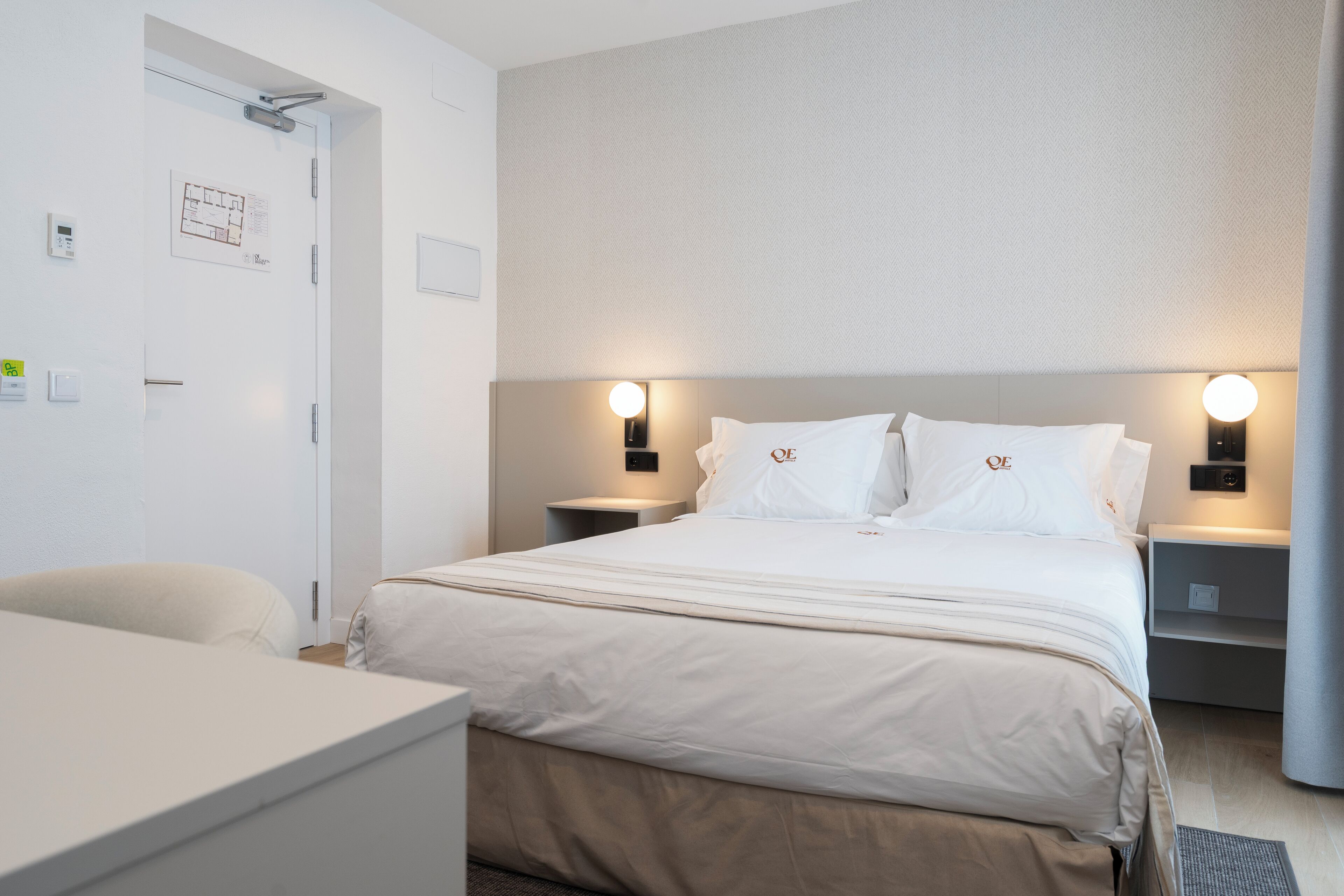 A hotel room with a bed, bedside tables, a desk, and a door.
