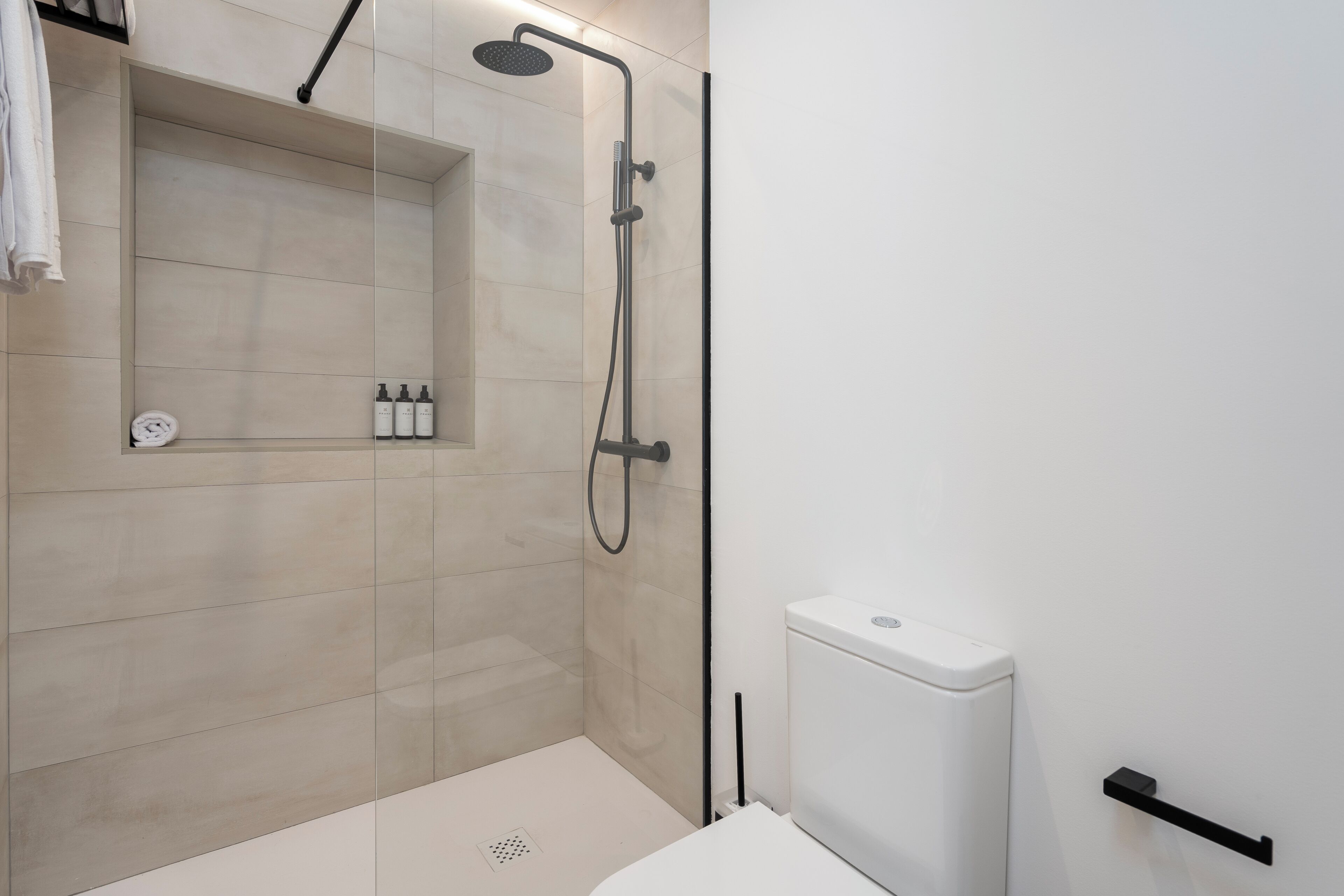 Un bagno moderno con doccia vetrata, un WC e uno scaffale con articoli da toilette.