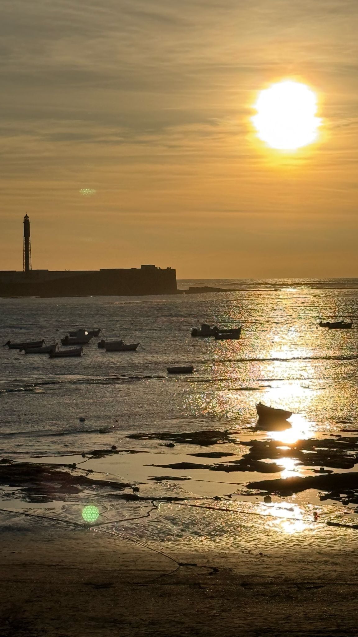A sunset over a body of water with boats and a lighthouse in the background.