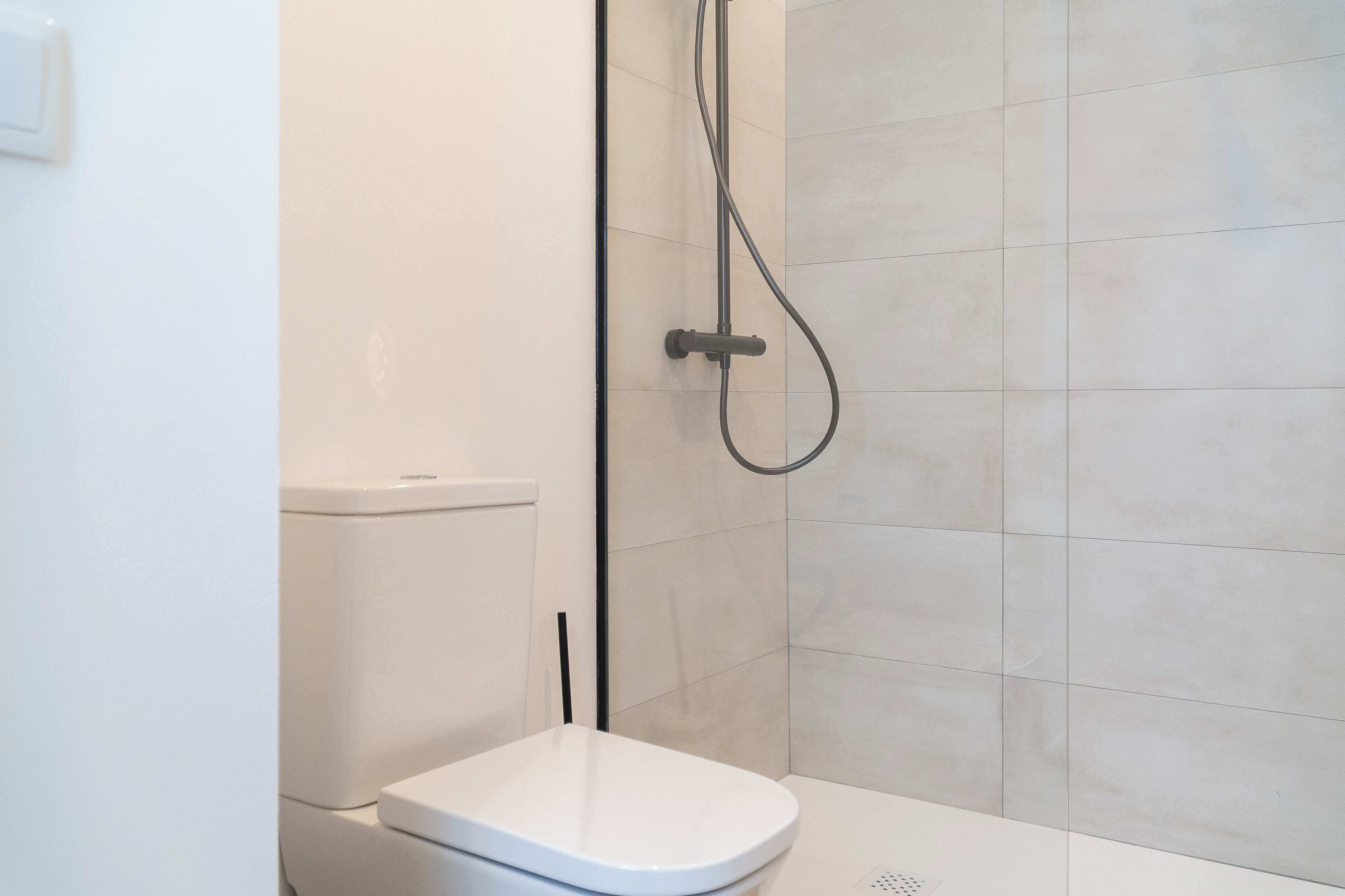 Un baño moderno con inodoro blanco, cabina de ducha y paredes de azulejos.
