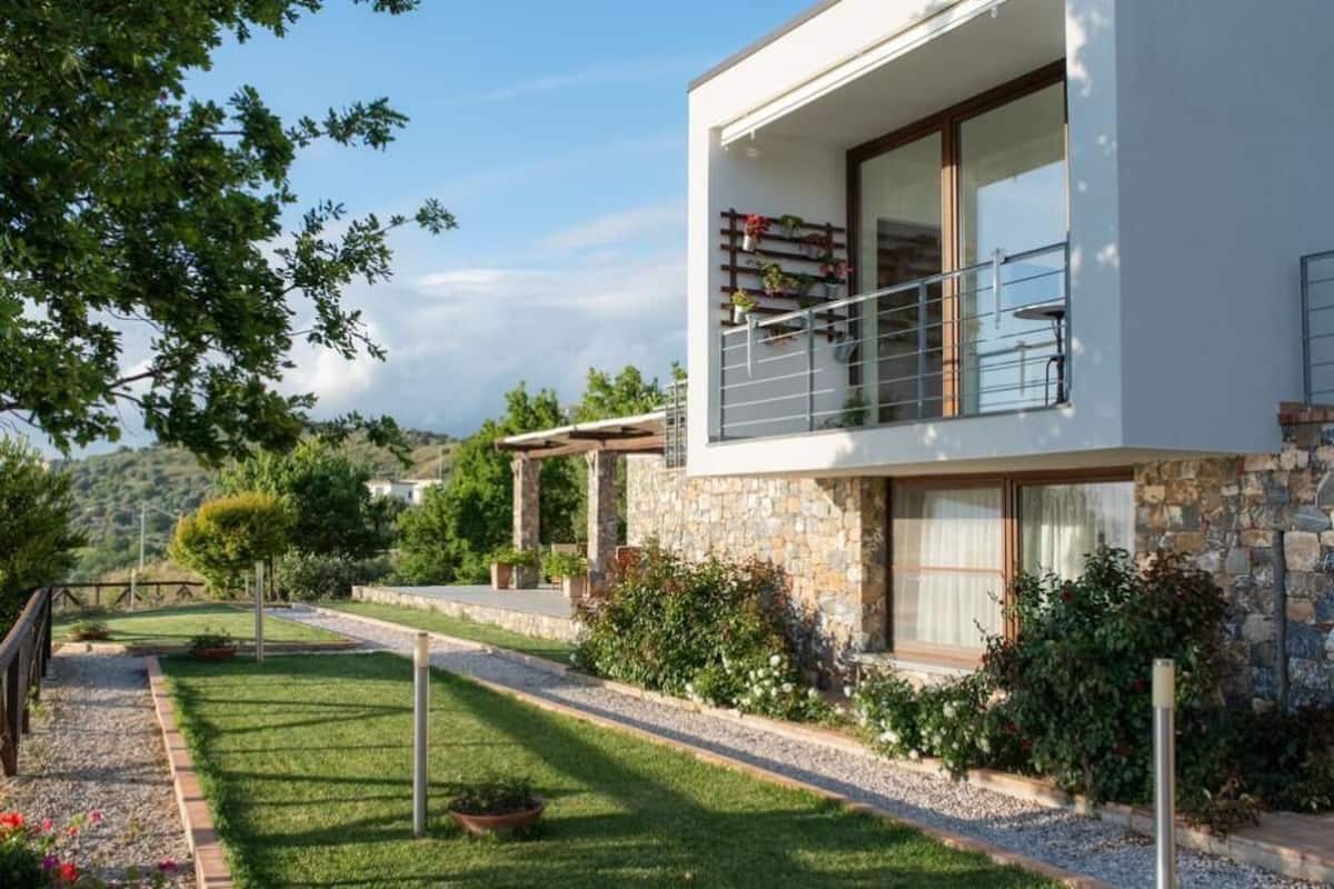 Une maison moderne à deux étages, dotée d’une façade en pierre, d’un balcon agrémenté de plantes en pot et d’un jardin bien entretenu.