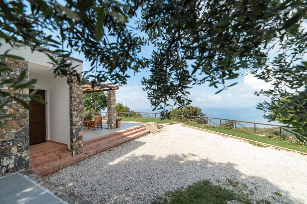 Una casa moderna con facciata in pietra, patio lastricato di ghiaia e pergola in legno.