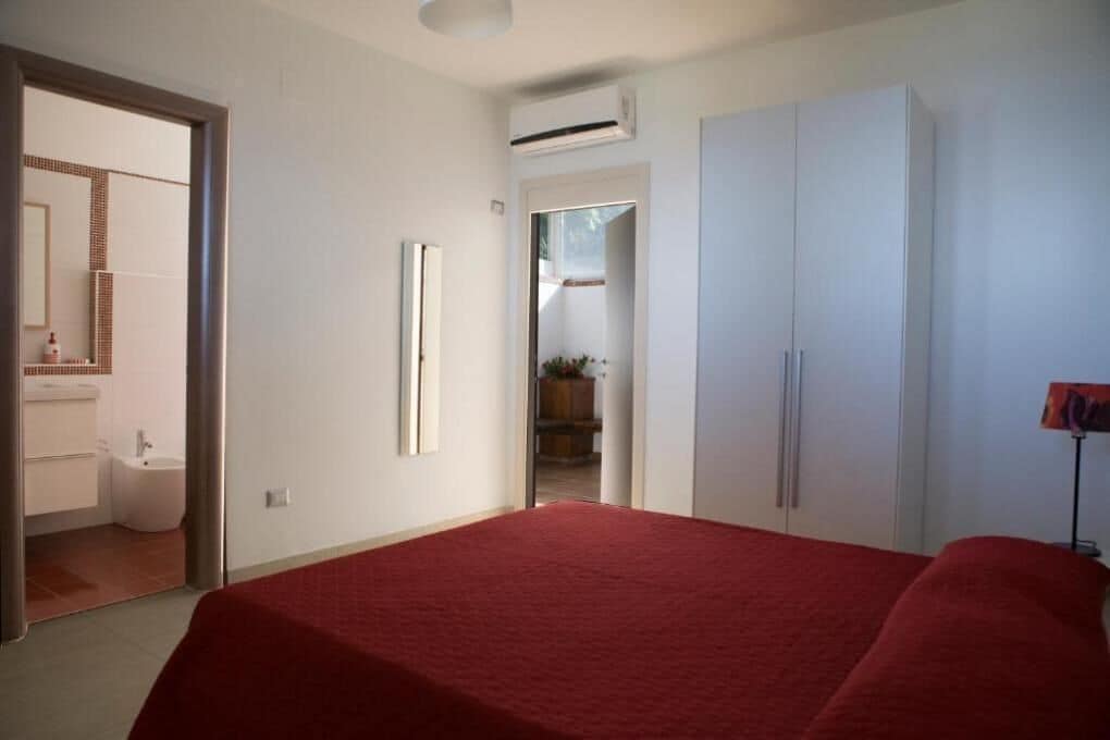 Una camera da letto con un letto, un armadio e un bagno visibile attraverso una porta aperta.