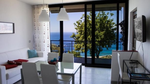 Ein modernes Wohnzimmer mit Glastisch, weißem Sofa und Meerblick.