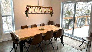 A dining area with a wooden table and chairs, a hanging light fixture, and large windows with a view of trees and a deck. - Spa & Breathtaking View | Le Dumont | Panorama (Saint-Philémon)