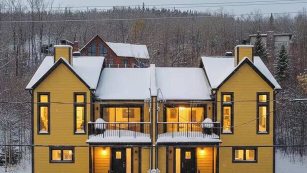 A two-story yellow building with a snow-covered roof, a balcony on the second floor, and a front entrance with steps leading up to it. - Spa & Breathtaking View | Le Dumont | Panorama (Saint-Philémon)