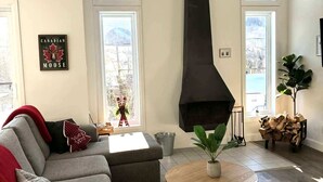 A modern living room with a fireplace, a sofa, a coffee table, and a large window. - Spa & Breathtaking View | Le Dumont | Panorama (Saint-Philémon)