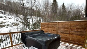 A hot tub on a wooden deck with snow on the ground and trees in the background.