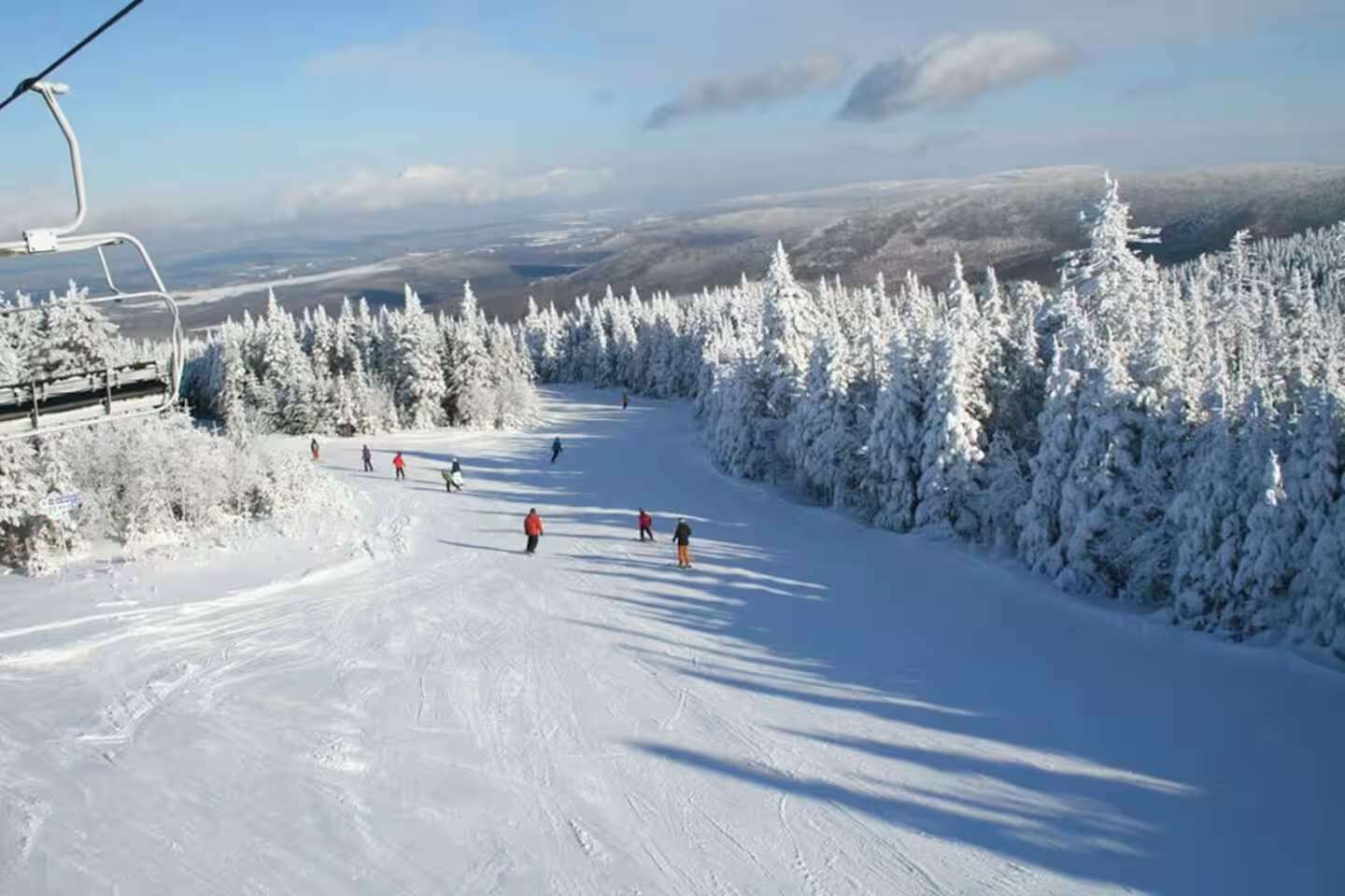 Eine Skipiste mit Seilbahn, schneebedeckten Bäumen und blauem Himmel.