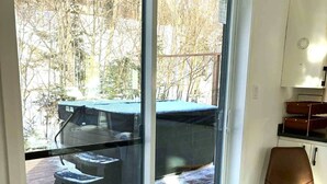 A room with a large sliding glass door leading to a covered outdoor area. Inside, there is a wooden table and a brown chair.