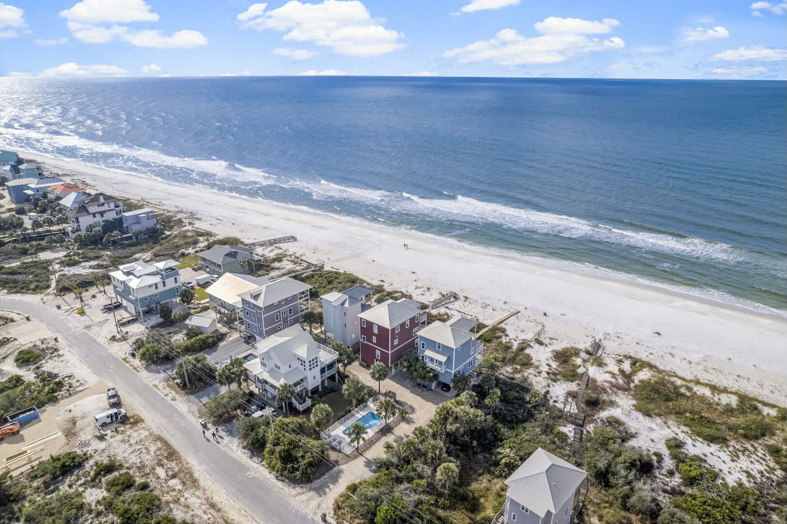An aerial view of a coastal residential area with houses near the beach, a clear sky, and the ocean in the background.