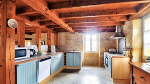 A kitchen with wooden beams, a stone wall, and a view of the outside. - Stone house at the foot of La Vézère, for 6 (Saint-Léon-sur-Vézère)