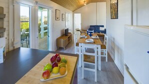 Une cuisine spacieuse dotée d’un plan de travail en bois, d’un coin repas avec des chaises blanches et d’une vue sur le jardin grâce à une porte-fenêtre coulissante.