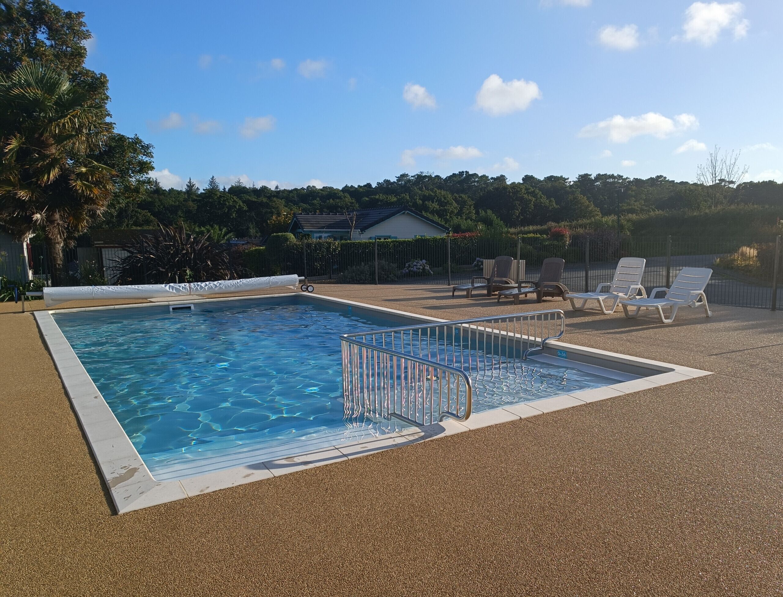 A rectangular swimming pool with a metal safety railing, surrounded by a textured gravel area.