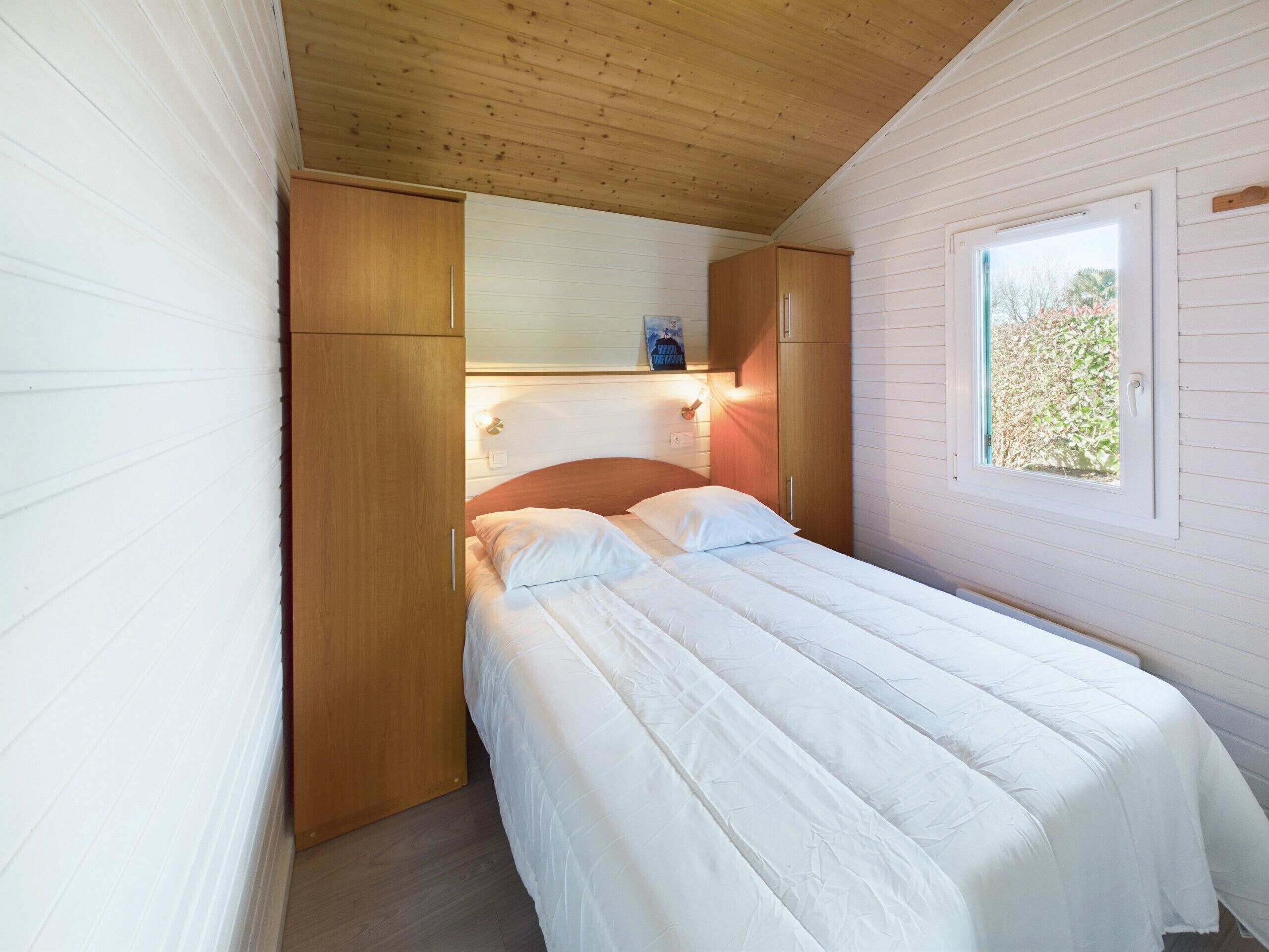 Una camera da letto con soffitto in legno, un letto con biancheria bianca, un armadio in legno e una finestra vista verde.