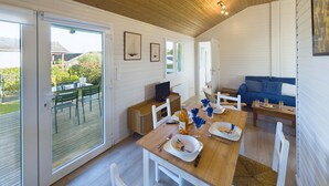 Une pièce spacieuse avec un plafond en bois, une table à manger dressée avec des assiettes et des couverts, un canapé et un téléviseur posé sur un meuble en bois.