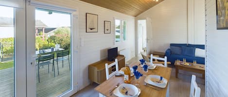 Ein geräumiges Zimmer mit Holzbalkendecke, einem Esstisch mit Geschirr und Besteck, einem Sofa und einem Fernseher auf einem Holzboden.