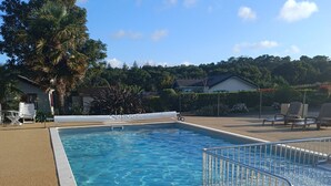 Une piscine rectangulaire à l’eau d’un bleu limpide, entourée d’une terrasse beige à la texture particulière.