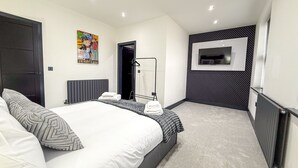 A modern bedroom with a large bed, a TV mounted on the wall, and a radiator. - Santi House (Boston)