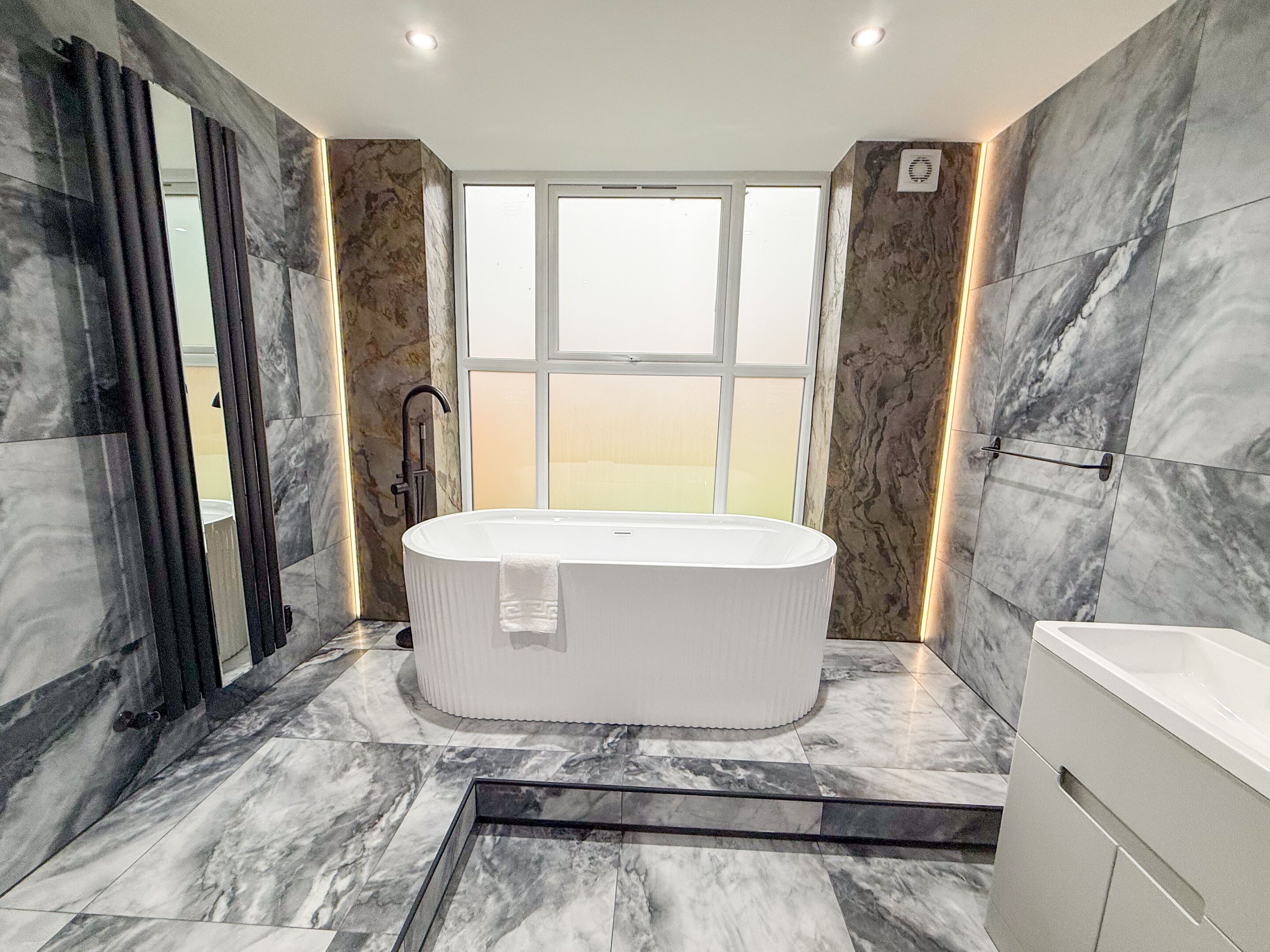 A modern bathroom with a freestanding bathtub, a shower area, and a large window providing a view.