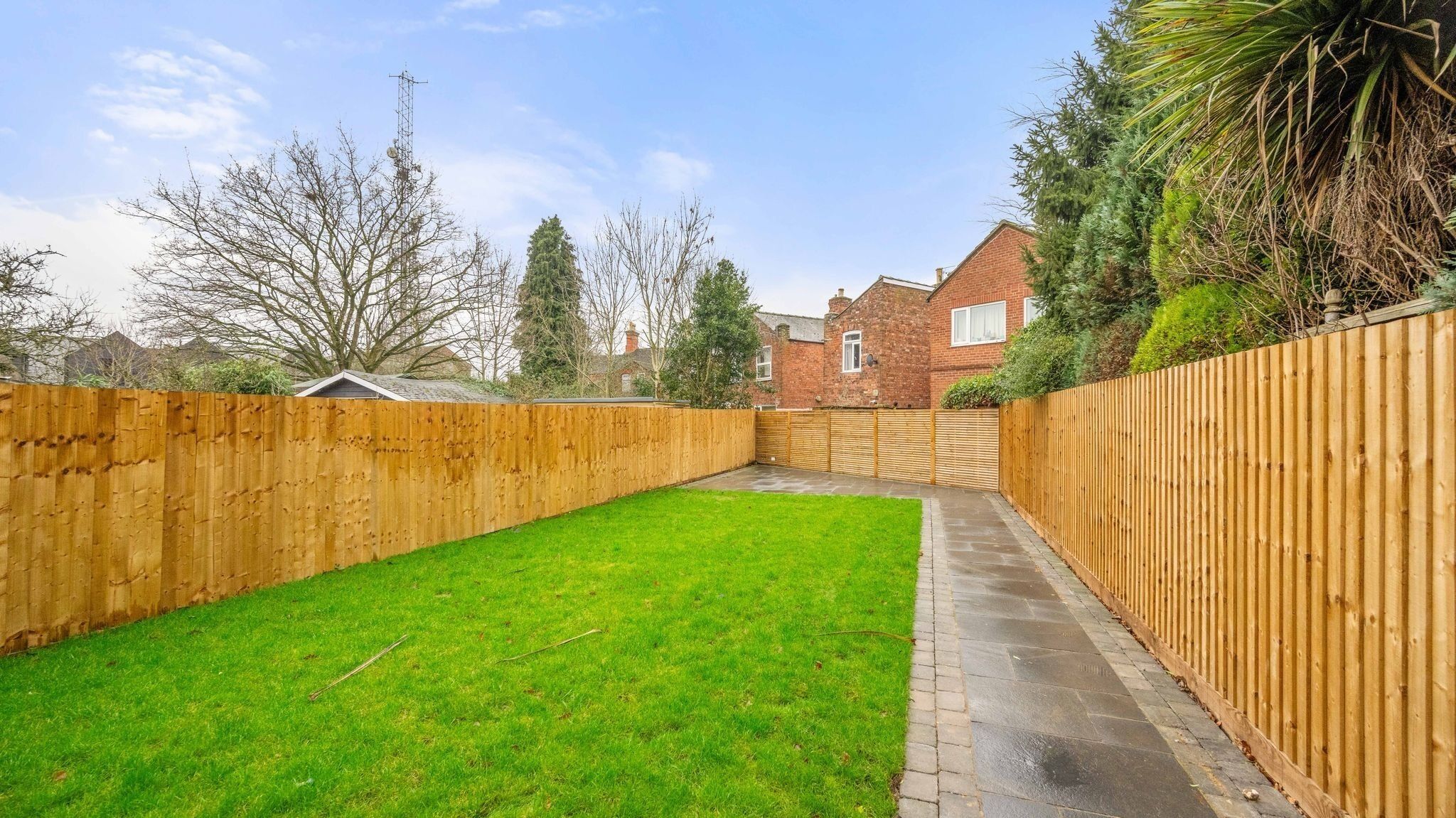 A backyard with a wooden fence, a paved pathway, and a grassy lawn.