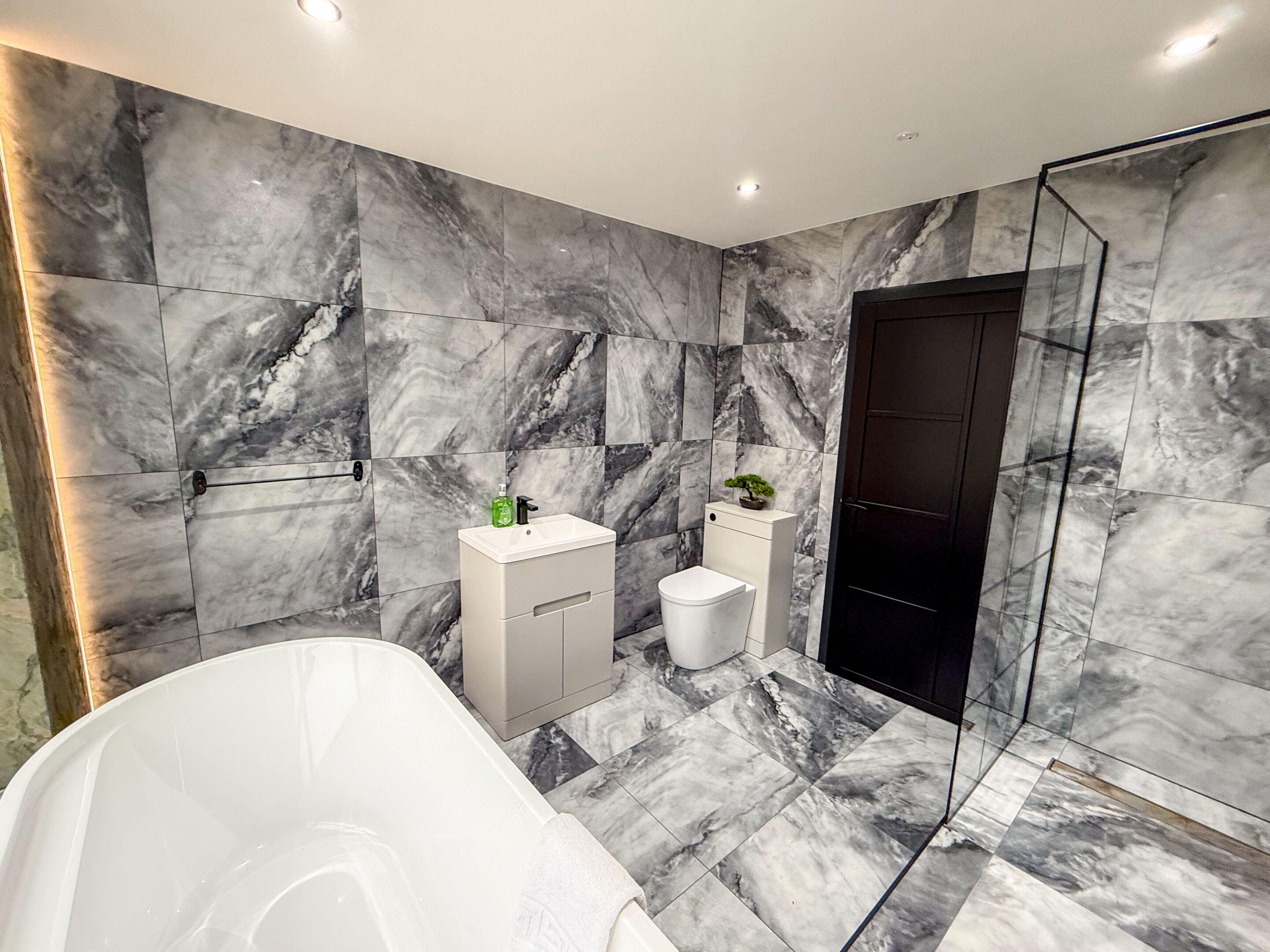 A modern bathroom with a bathtub, a sink, and a toilet, all set against a marble wall.