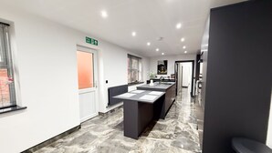 A modern kitchen with a central island, a fire exit sign, and a hallway leading to other rooms. - Santi House (Boston)