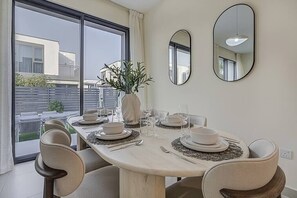 Enjoy meals with a view from this dining area, featuring a round table for six and large windows overlooking the balcony and surrounding buildings.