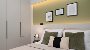 A modern bedroom with a bed, two pillows, a nightstand with a lamp, and three framed pictures on the wall.