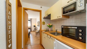 A modern kitchen with a microwave, oven, and sink. There is a wooden door with a sign, a potted plant, and a rug on the floor. - Dreamlike apartment house on the lakeshore port side (Waren (Müritz))