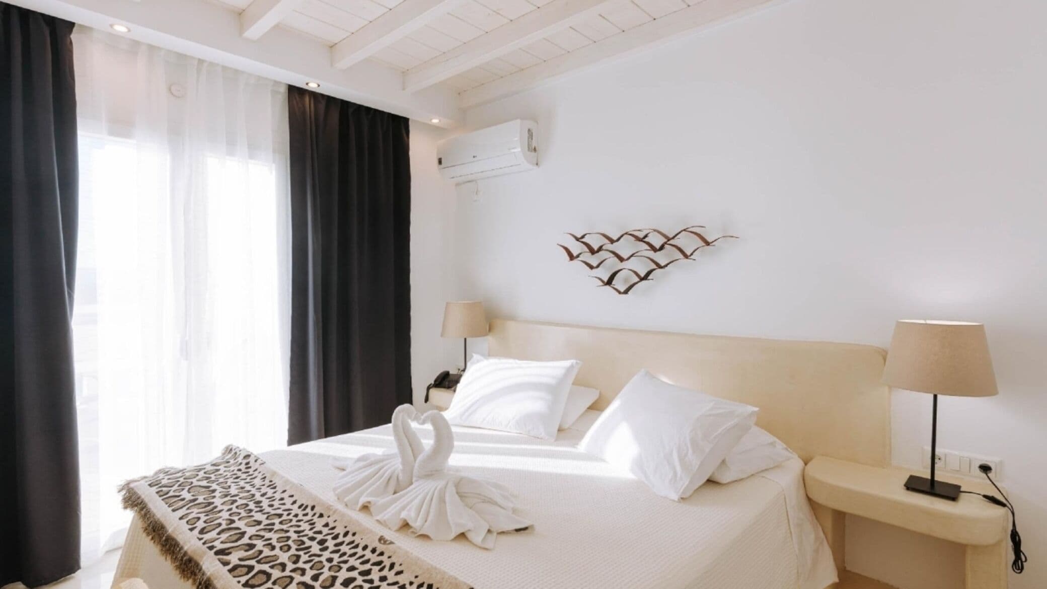 Habitación de hotel con cama, dos mesitas de noche, aire acondicionado de pared y un adorno mural.