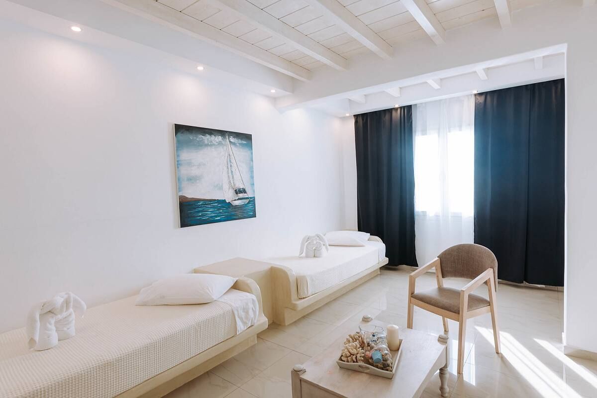 Een hotelkamer met twee enkele bedden, een klein tafeltje met decoratieve objecten, een stoel en een schilderij van een zeilboot aan de muur.