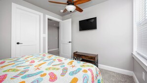 Une chambre à coucher avec un lit, un ventilateur de plafond, une télévision et un bureau.