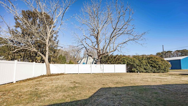 Une cour arrière avec une clôture blanche, un arbre et un bâtiment bleu en arrière-plan.