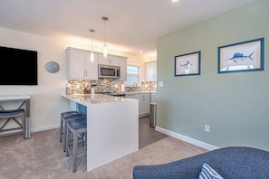 A modern kitchen with a central island, bar stools, a microwave, and a sink. - "Marlin Sunset" - 11th/Bay, 2 BRs, sleeps 6 (Ocean City)