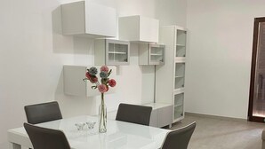 Een moderne eetruimte met een witte tafel en stoelen, een vaas met bloemen en ingebouwde kasten.