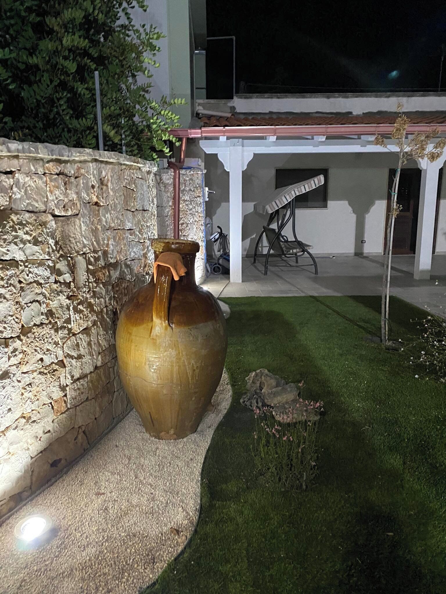 Eine Steinsäule, eine große Vase und eine Terrasse mit Tisch und Stühlen.