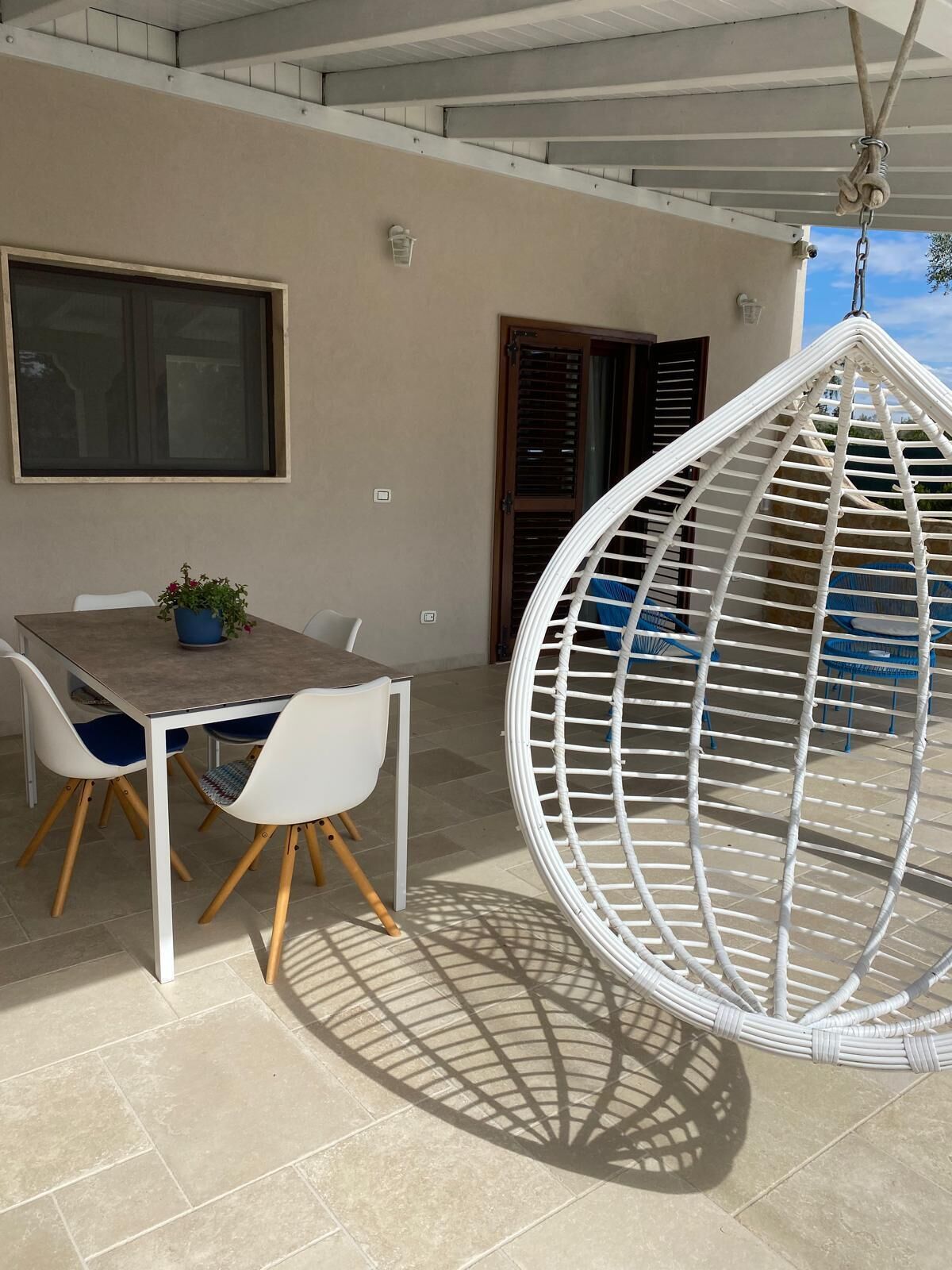 Un patio con una mesa redonda y sillas, una silla colgante y un ventanal.