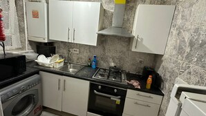 Una cocina compacta con armarios blancos, estufa a gas, microondas y lavadora.