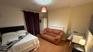 Una habitación de hotel con una cama, un sofá de cuero marrón, una mesita con una lámpara y una luz en el techo.