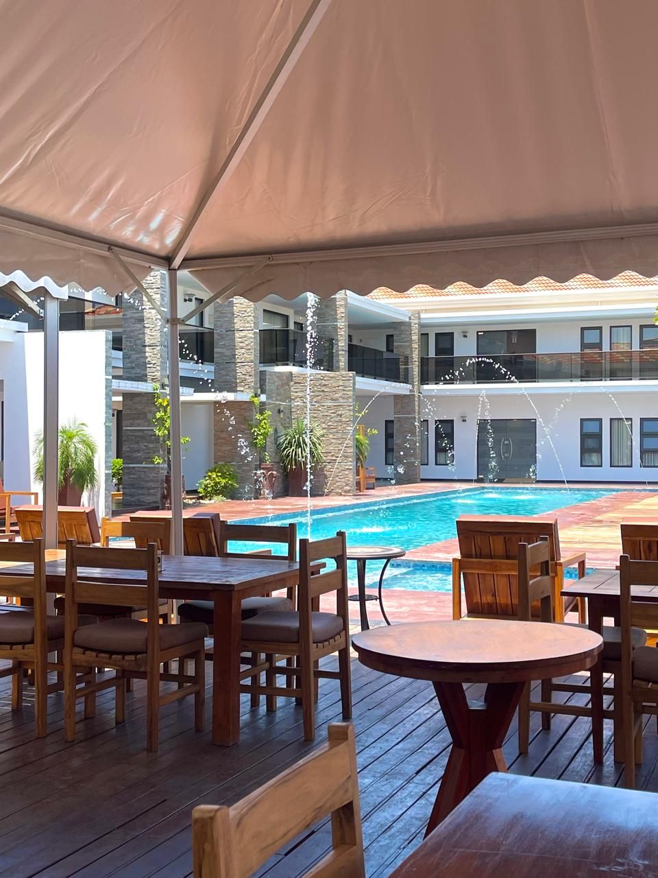 Un espace piscine extérieur avec des tables et des chaises en bois, entouré d’une terrasse couverte.