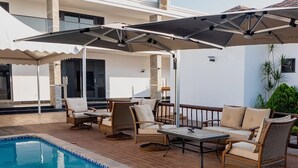 A poolside area with wicker furniture, a table, and umbrellas providing shade. - Platinum Lodge (Matola)