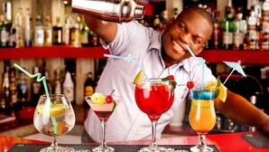 A bartender pouring a drink into a martini glass, with three other drinks on the counter. - Platinum Lodge (Matola)