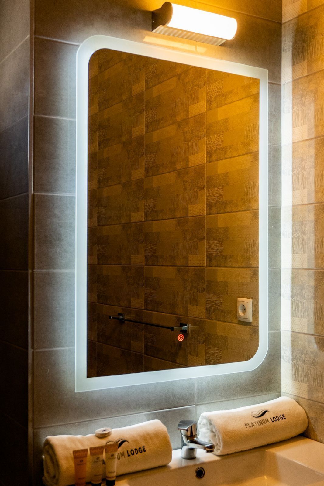 Ein Badezimmer mit einem großen Spiegel, einer Dusche und einem Waschbecken. Auf dem Waschbecken liegen Handtücher und Toilettenartikel.