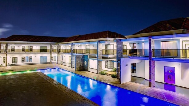 A modern hotel with a swimming pool, multiple balconies, and a well-lit facade. - Platinum Lodge (Matola)