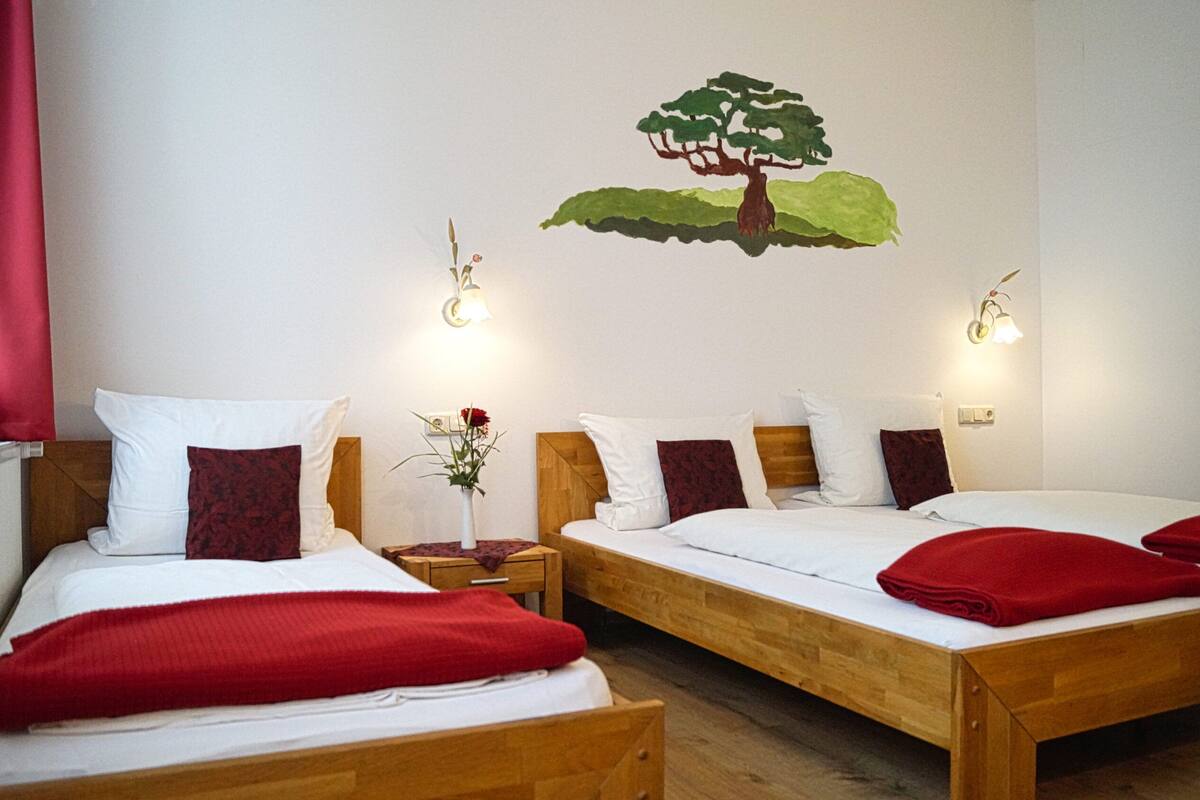 A hotel room with two wooden beds, white bedding, red pillows, and a wall mural of a tree.