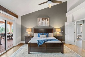 A bedroom with a large bed, two bedside tables with lamps, a ceiling fan, a painting on the wall, and a view through a sliding glass door. - 5 Bed, 3 Bath Uptown Sedona-Game Room-Sauna-Cold Plunge-Jacuzzi-Gym (Sedona)